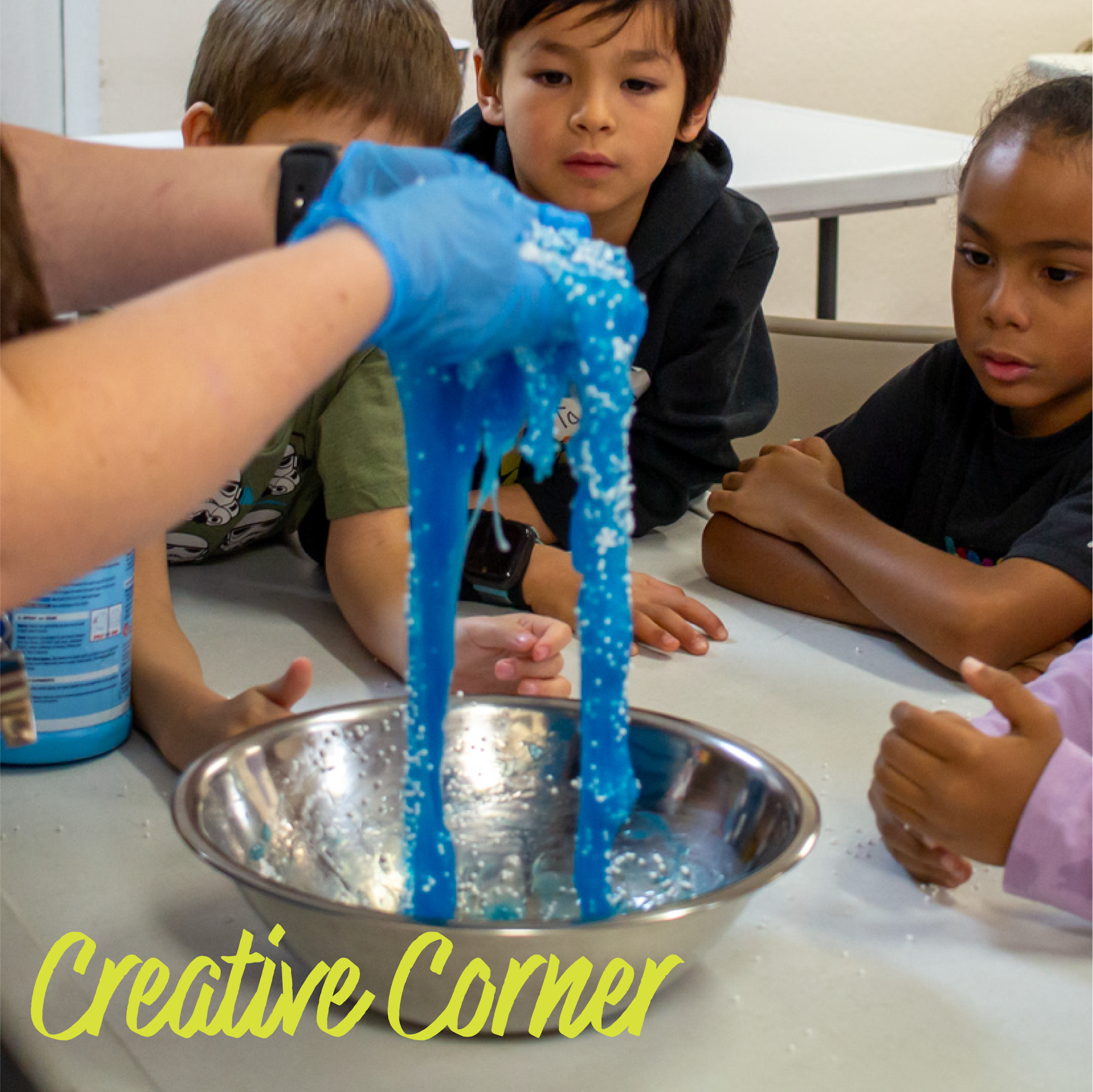 A person making blue slime in a bowl, surrounded by children watching intently. Text reads "Creative Corner."