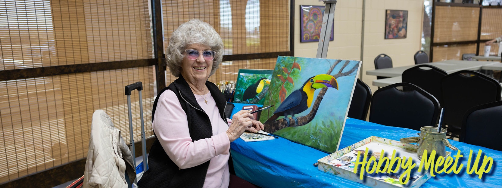 A person smiling and painting a toucan at a hobby meetup event.