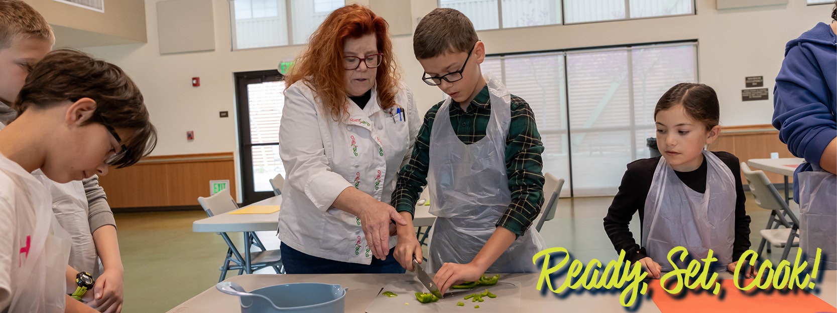 People in a cooking class, slicing vegetables. Text: "Ready, Set, Cook!"