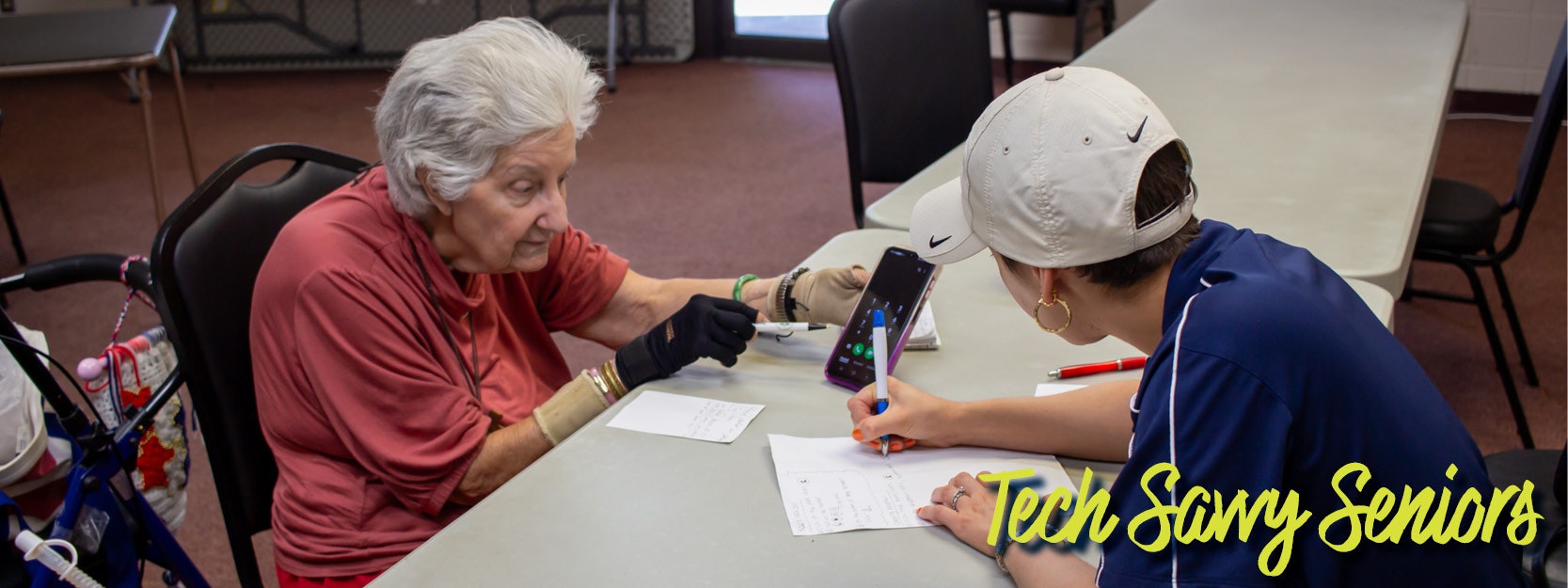 An elderly woman learns about a smartphone from a helper; "Tech Savvy Seniors" text is present.