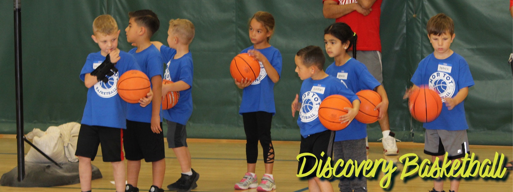 Kids in blue shirts hold basketballs in a gym, with "Discovery Basketball" text.