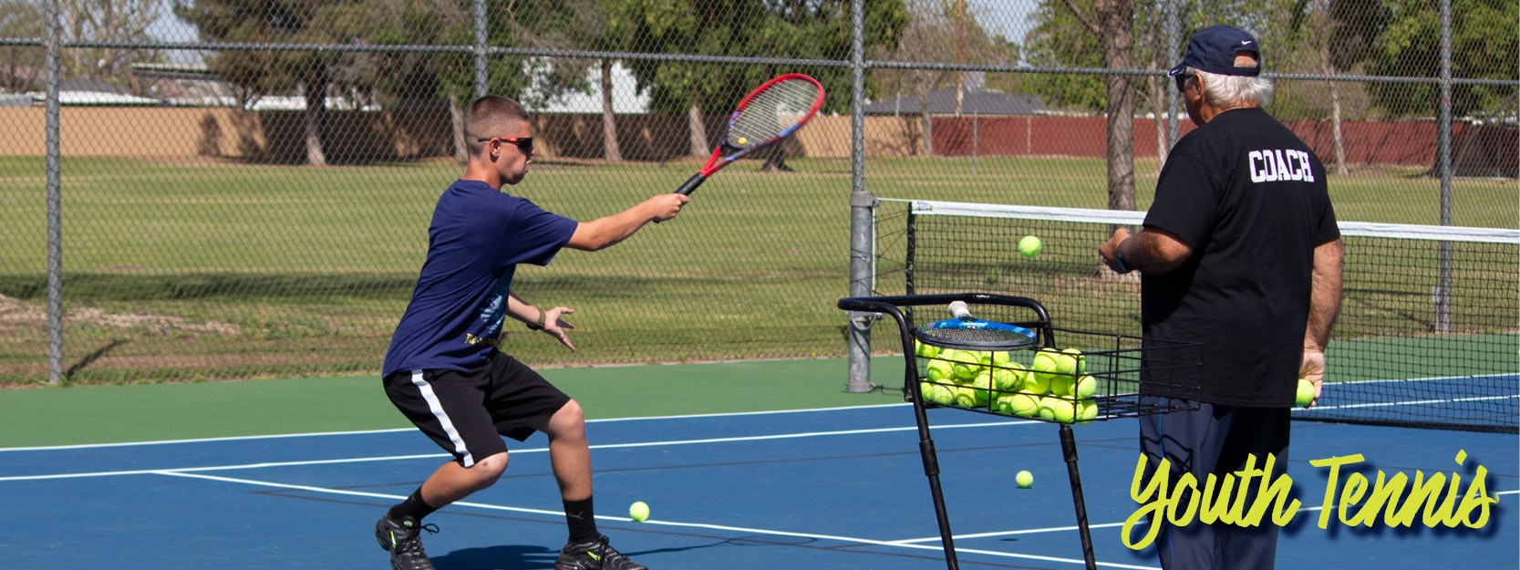 A young player hits a tennis ball as a coach oversees, on a court with a ball cart. Text reads "Youth Tennis."