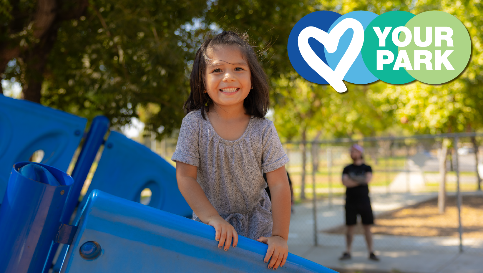 Happy child on playground equipment with a "Love Your Park" graphic and a person in the background.