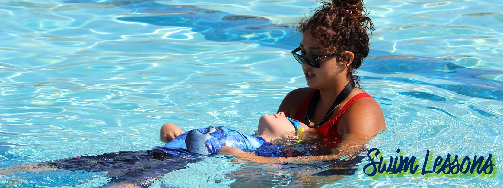 A swimming instructor is helping a child float on their back in a pool, with "Swim Lessons" written in the corner.