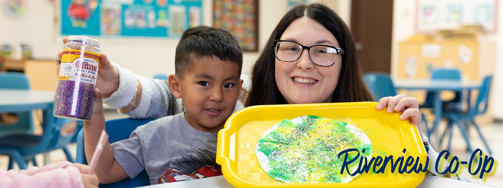 A child and adult in a classroom, holding glitter and a tray with a colorful art project. "Riverview Co-Op" text is visible.