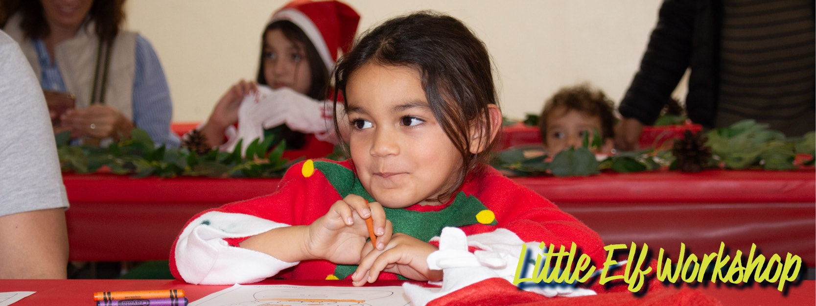 A child dressed as an elf sits at a table with a drawing, crayons, and holiday decorations. Text: "Little Elf Workshop."