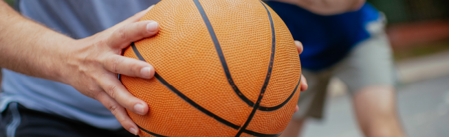 Two people playing basketball outdoors, one holding the ball.