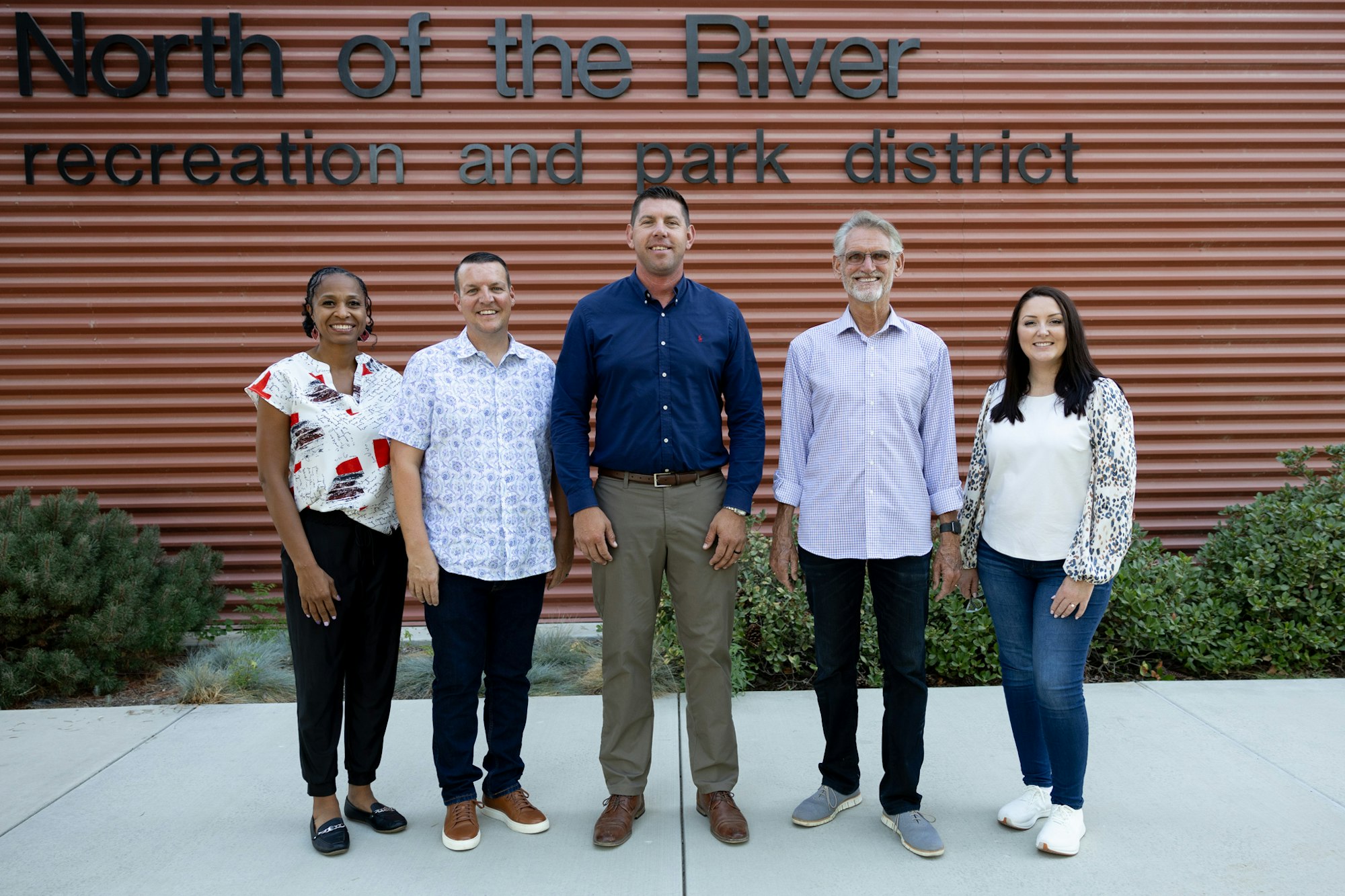 Five people posing in front of a sign saying "North of the River recreation and park district".