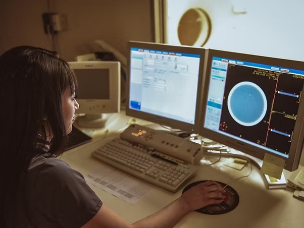Person analyzing medical imaging data on dual computer monitors.