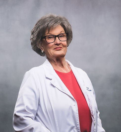 An older woman wearing glasses and a white coat over a red shirt, posing against a gray background.