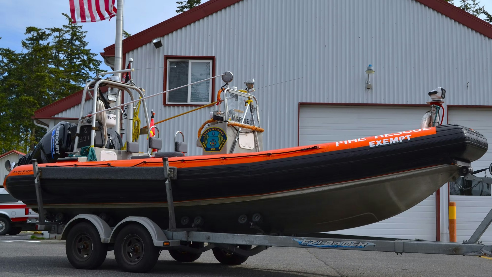 A fire rescue boat on a trailer, parked in front of a building with an American flag.