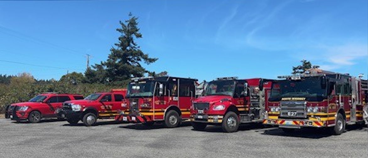 Five red emergency vehicles, including fire trucks and SUVs, parked in line under a clear blue sky.