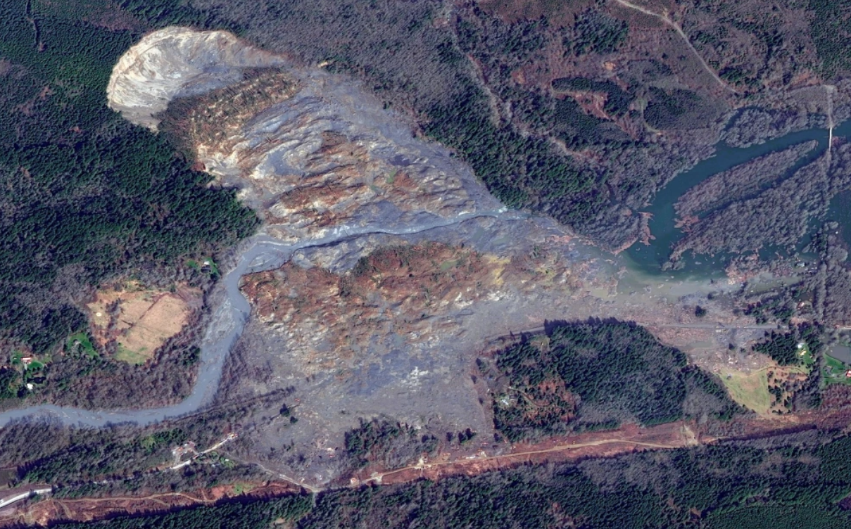 Aerial view of a large landslide and its path through a forested area, with visible debris and altered landscape.