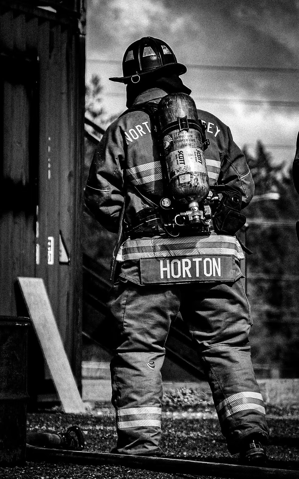 A firefighter in full gear with an oxygen tank, standing next to a building.
