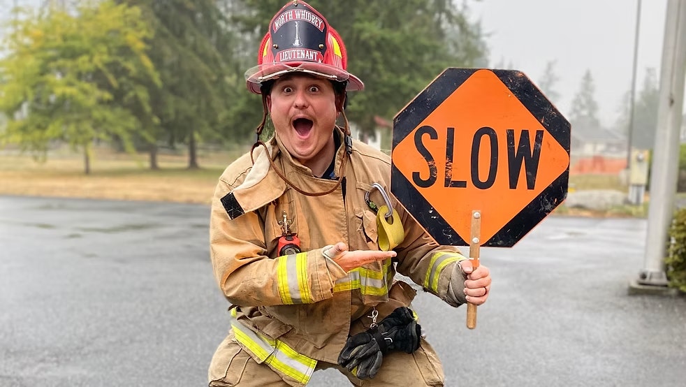 A firefighter excitedly points to an orange "SLOW" sign outdoors.