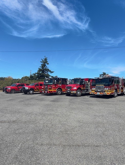 Fire trucks and red vehicles parked in an outdoor lot under a blue sky.