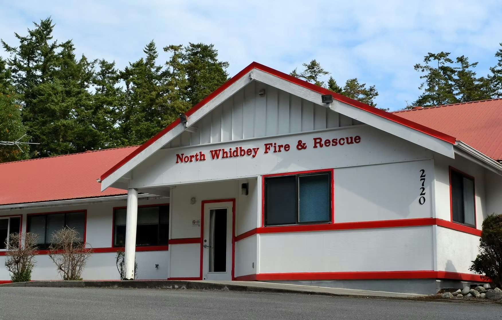 Building labeled "North Whidbey Fire & Rescue" with a red roof and trim, surrounded by trees.