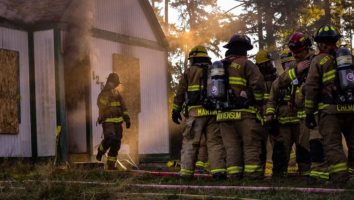 Firefighters in gear outside a smoky building, preparing to enter and manage a fire situation.
