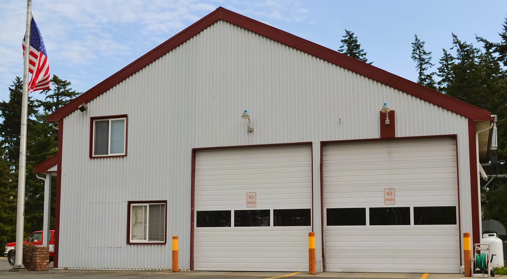 A metal garage with two closed doors, "No Parking" signs, and an American flag nearby.