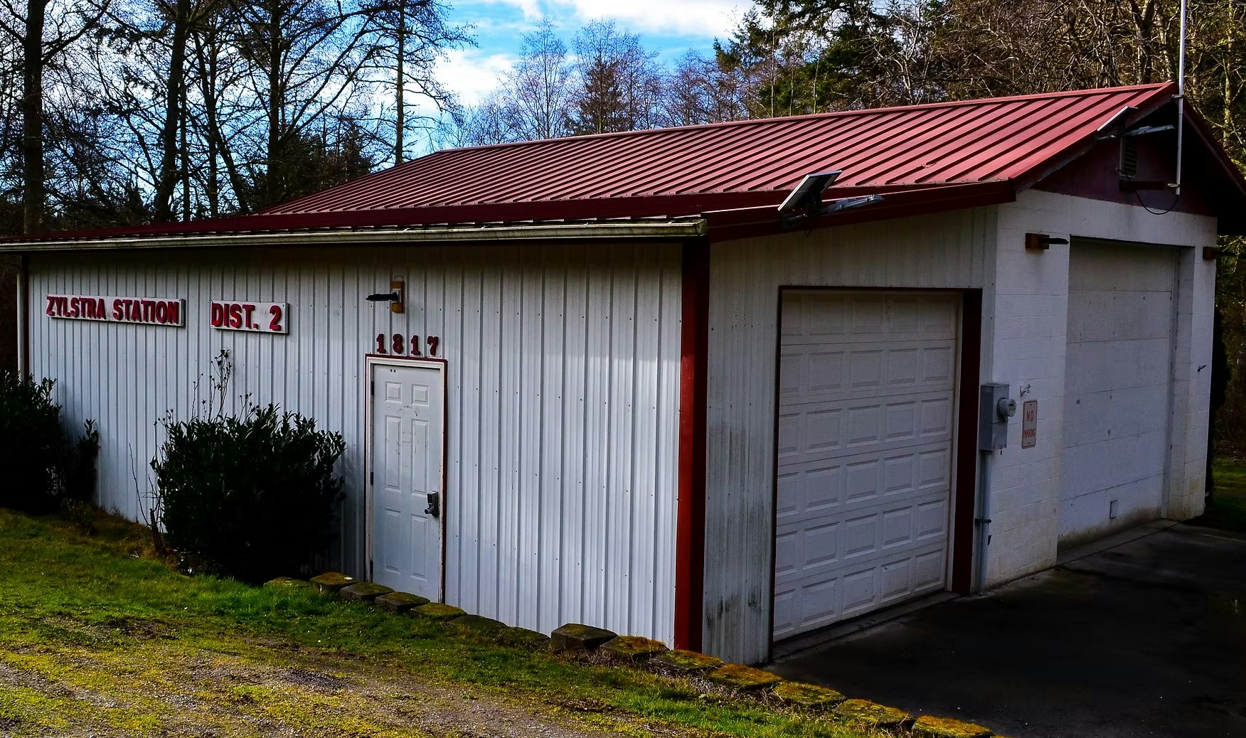 Small building labeled "Zylstra Station Dist. 2" with a red roof, white walls, and garage doors.