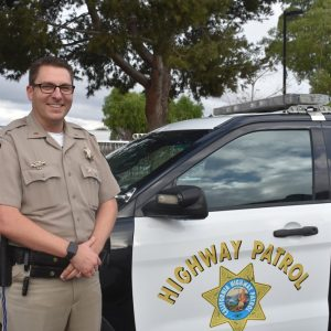 A smiling officer standing beside a highway patrol vehicle.