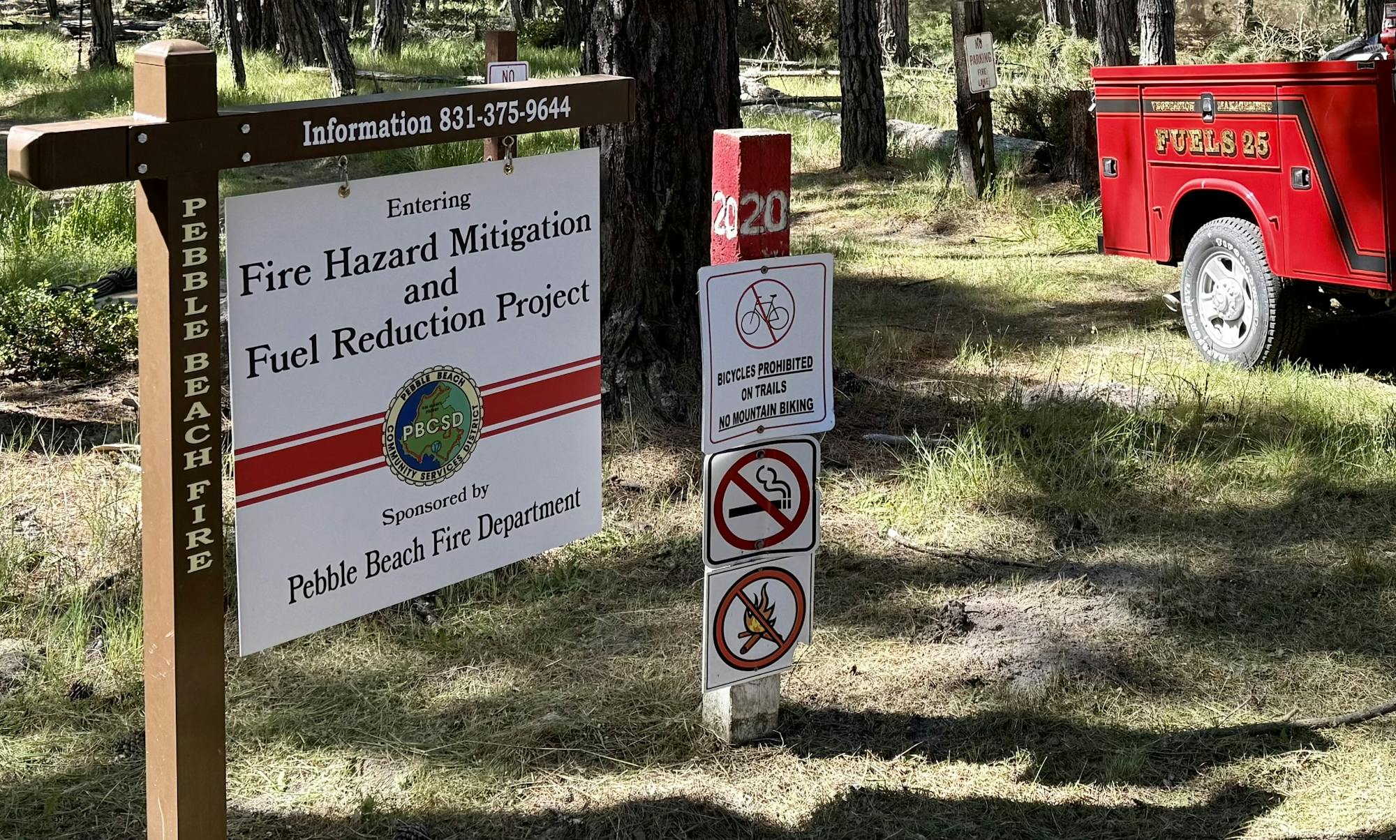 Forest entrance sign for fire hazard mitigation project; no biking or smoking allowed, with a fire department vehicle nearby.