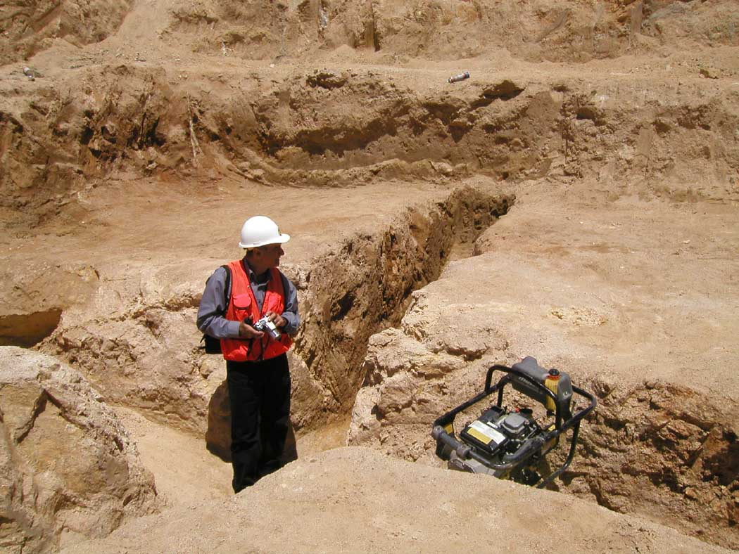 A person with a hard hat at an excavation site with equipment.