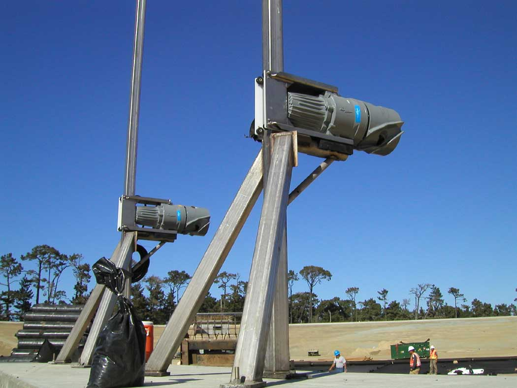 Dual outdoor floodlights on a pole, clear sky, some people and construction materials in the background.