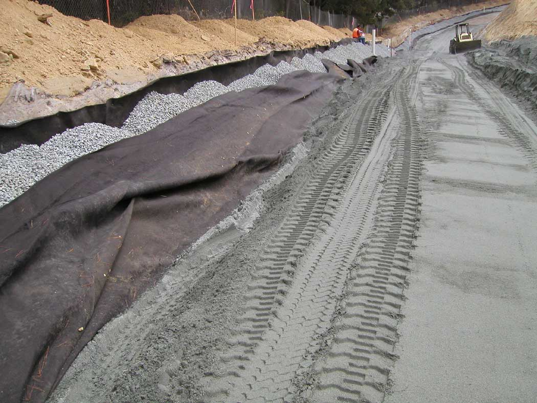 Road construction with geotextile fabric, gravel, and tire tracks from construction machinery.
