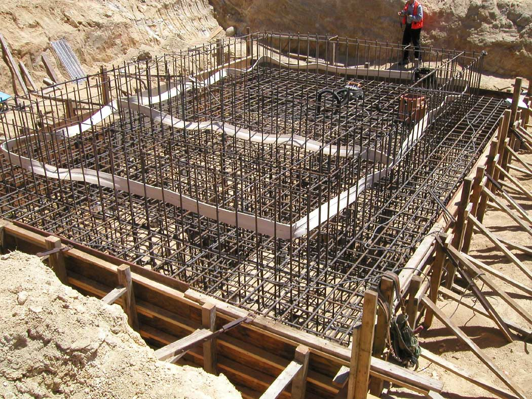 Concrete foundation framework with rebar and a worker on a construction site.