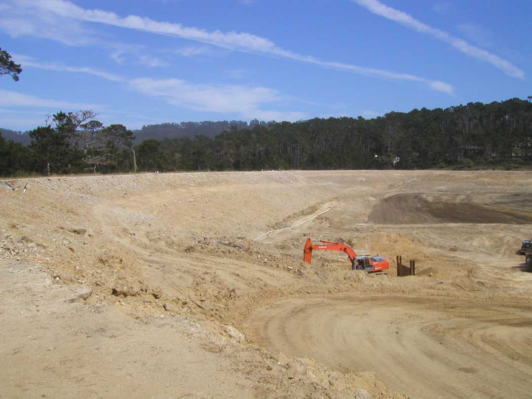 Construction site with an excavator, clear skies, and trees in the background.