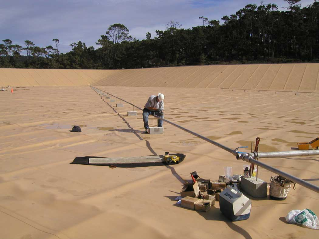 A worker applying a coating on a large, flat surface with tools and materials around.