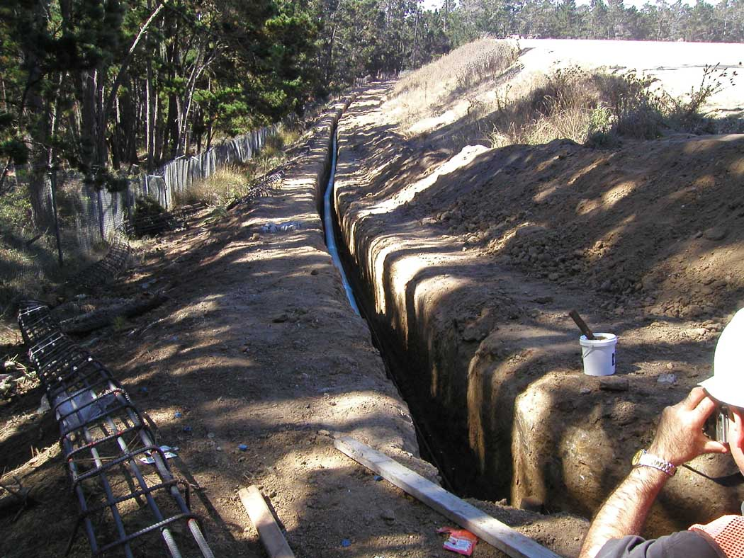 A deep trench under construction with reinforcing bars, indicating preparations for concrete work, possibly for foundations or pipelines.