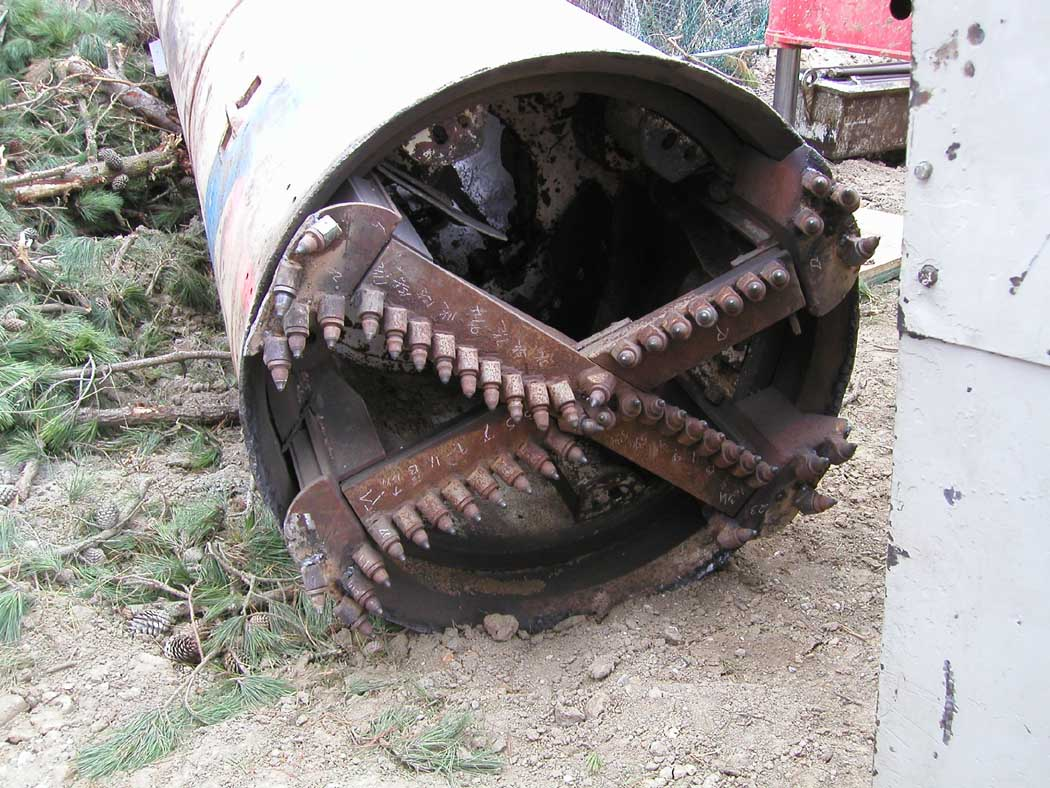 A close-up of a tree debarking or logging machine with metal teeth, surrounded by cut branches.