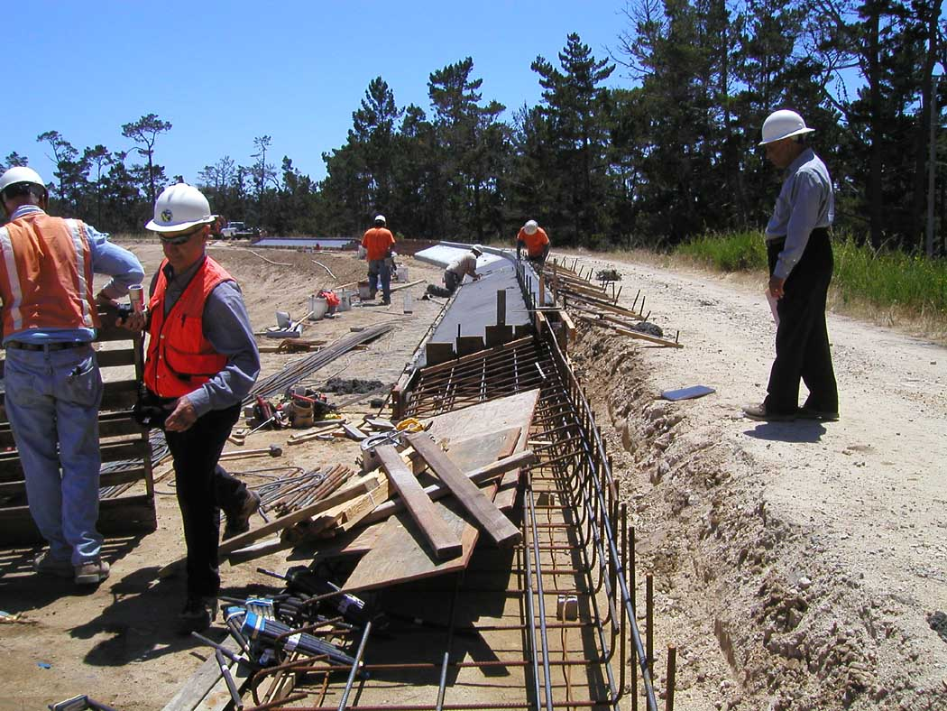 Construction workers with safety helmets at a site with rebar and wooden planks.