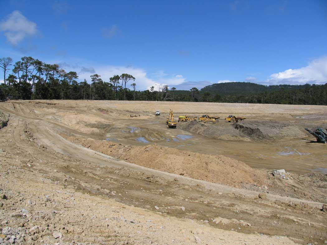 A construction site with heavy machinery, excavation in progress, under a clear sky.