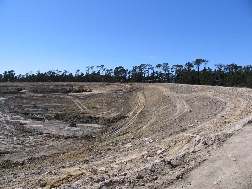 A construction site with deforested land and track marks under a clear sky.