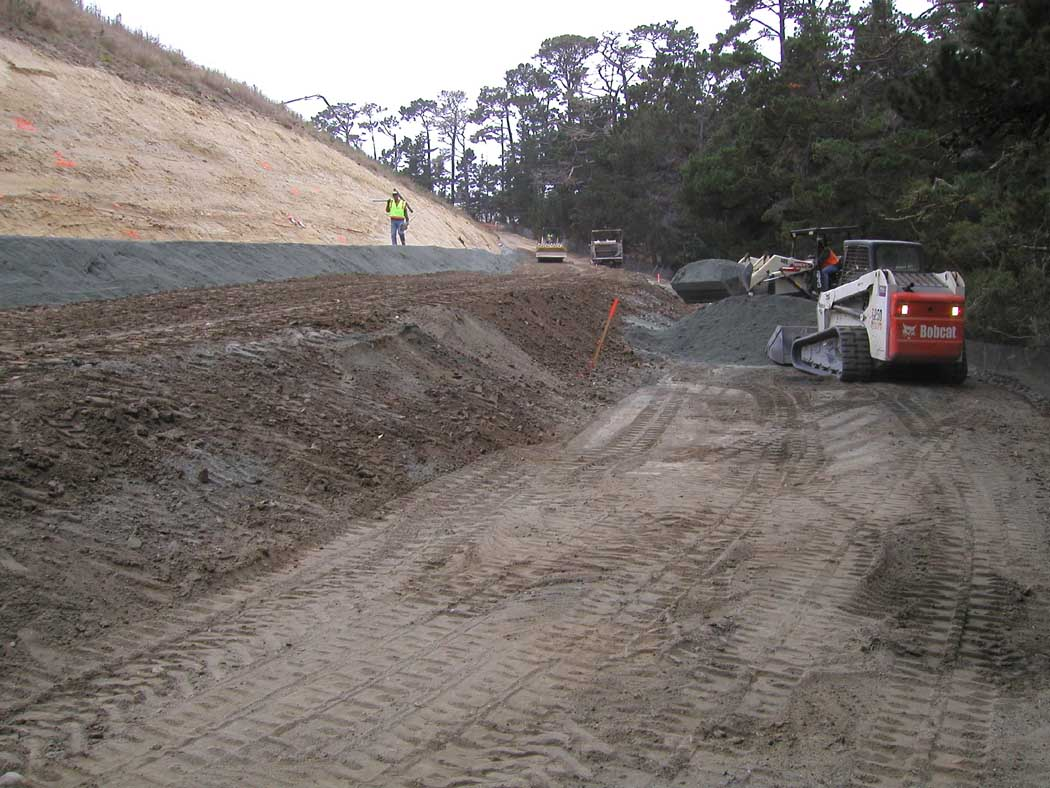 A construction site with heavy machinery and a worker wearing a safety vest.