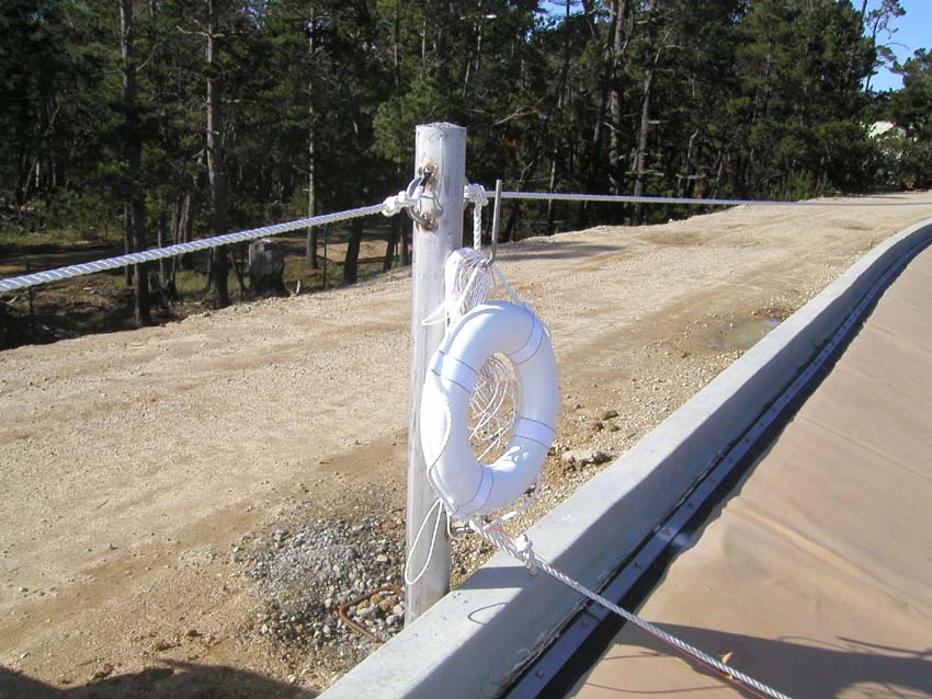 A lifebuoy attached to a fence near a dusty road with trees in the background.