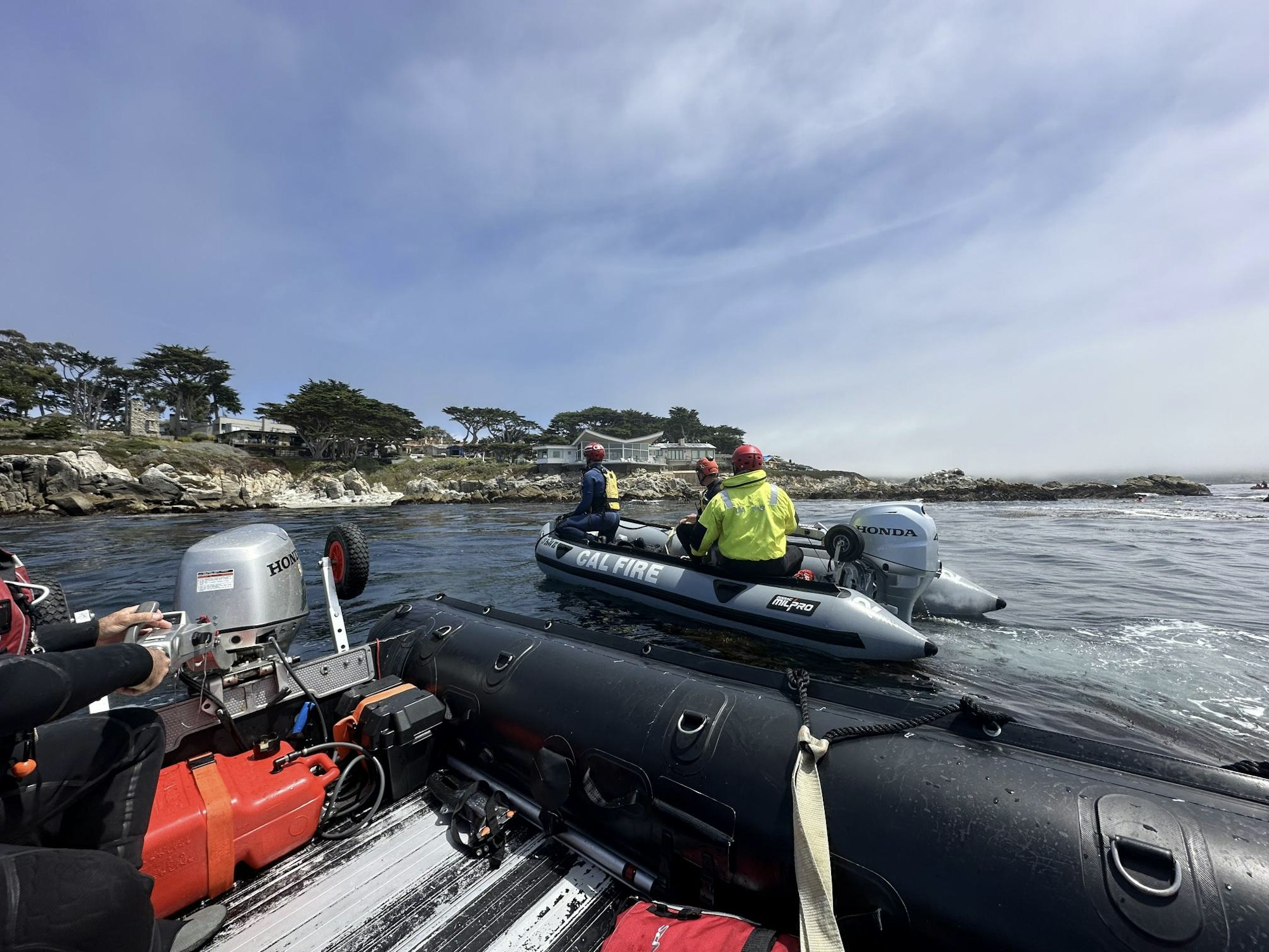 Two small boats on the water near a rocky shoreline, with people in gear. One boat labeled "Cal Fire."