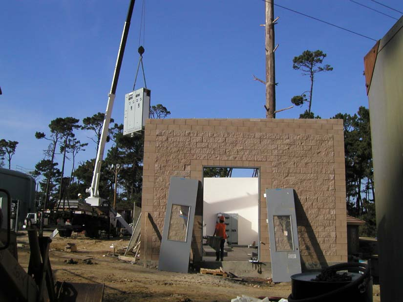 Construction site with crane lifting equipment, partial brick wall structure, and worker.