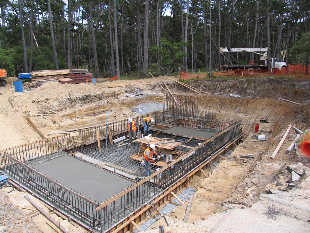 Construction site with workers, excavated ground, and reinforcement bars for concrete.