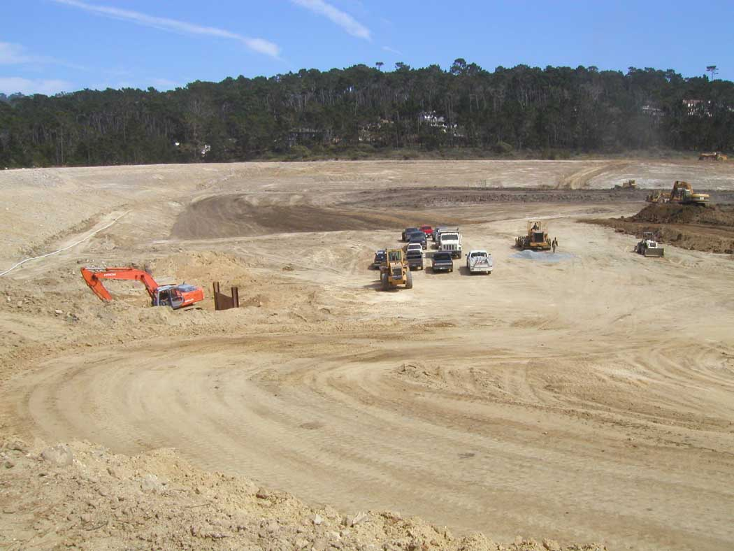 A construction site with heavy machinery and vehicles on dirt terrain, possibly preparing ground for development.