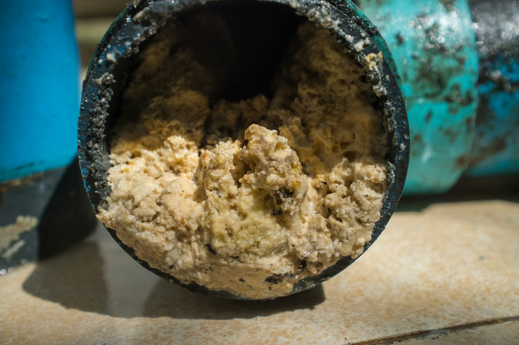 A close-up of a black pipe showing a buildup of a thick, beige substance, likely debris or sludge inside.