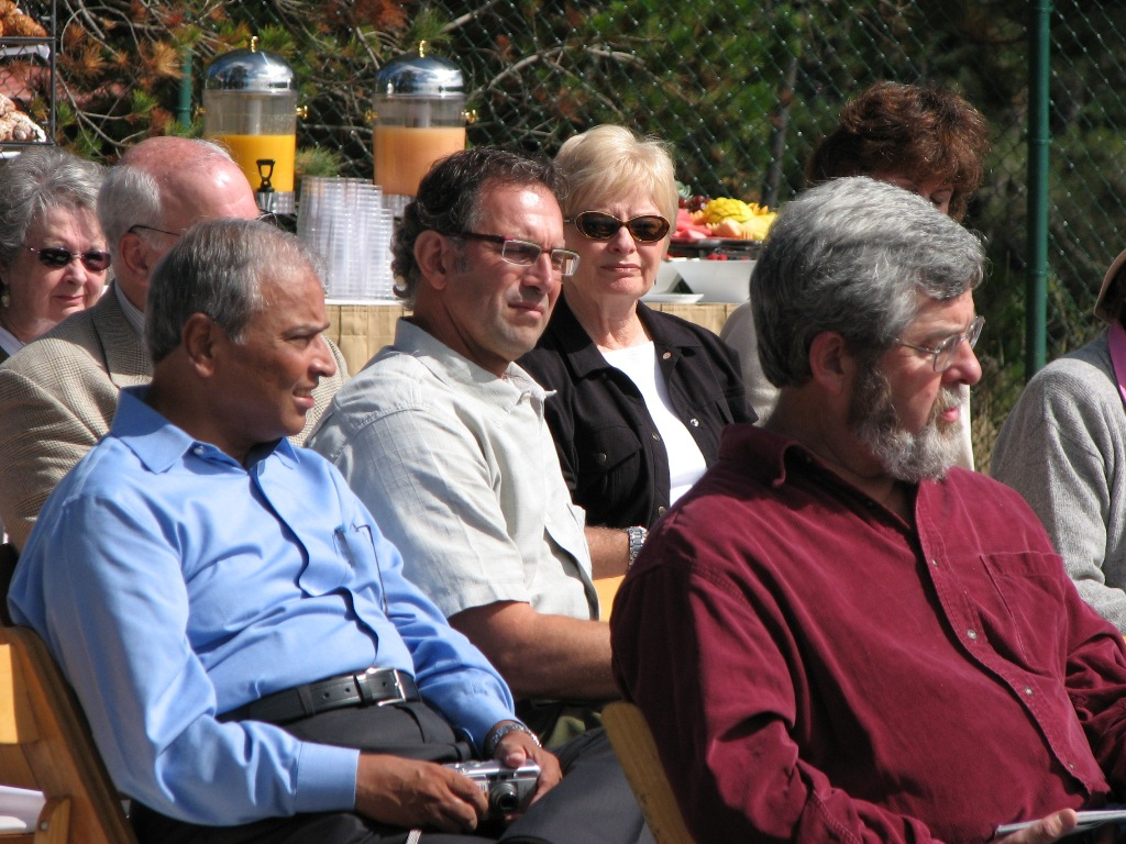 Group of people sitting outdoors, possibly at an event, with beverages served in the background.