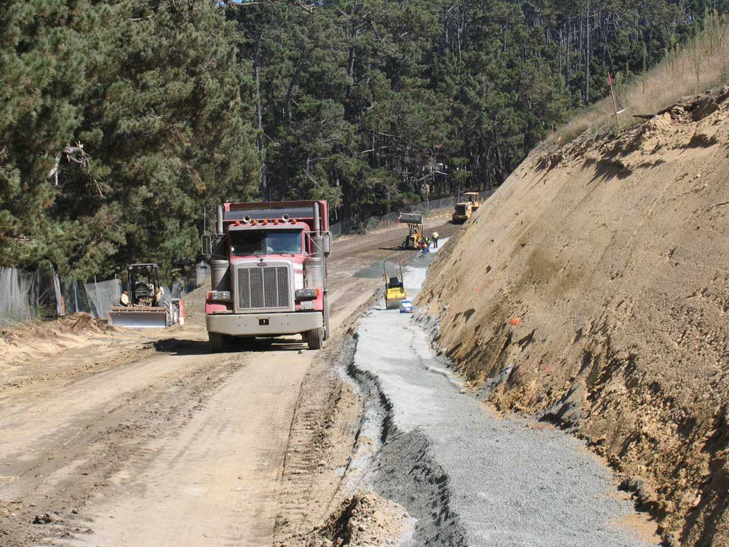 A road under construction with heavy machinery and a dump truck.