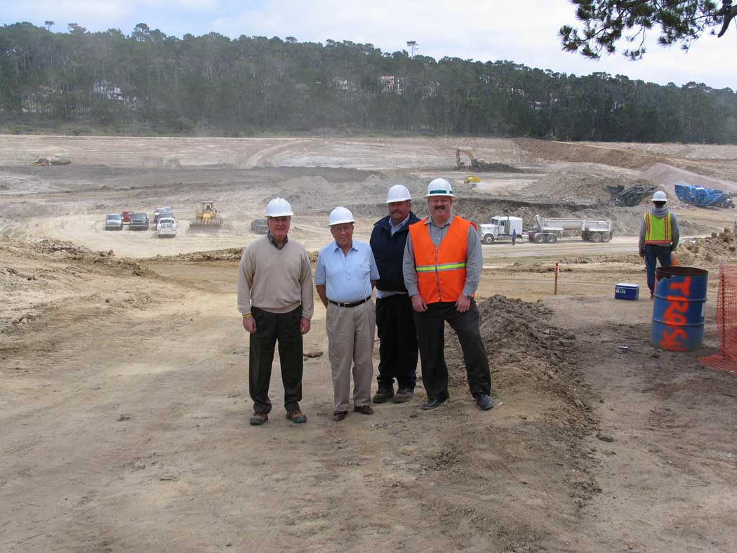 Four men in hard hats at a construction site with heavy machinery in the background.