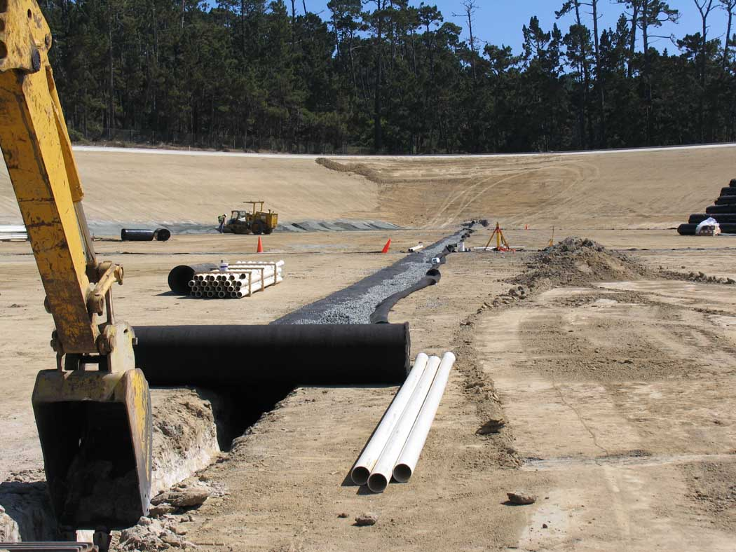 Construction site with excavator, large pipes, and machinery on cleared land.