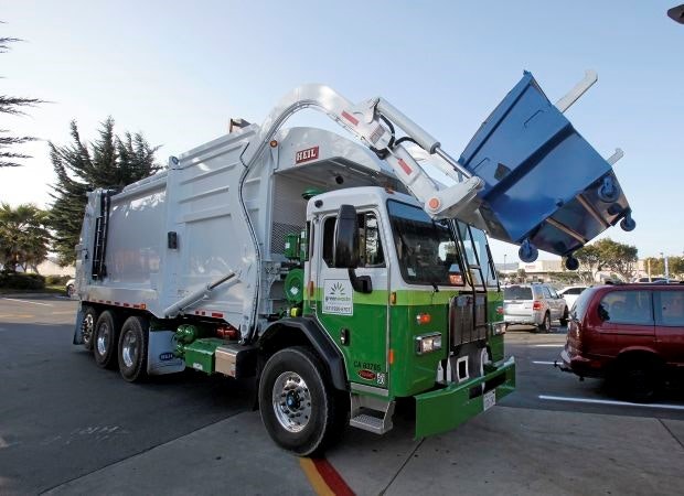 A garbage truck lifting a blue dumpster.