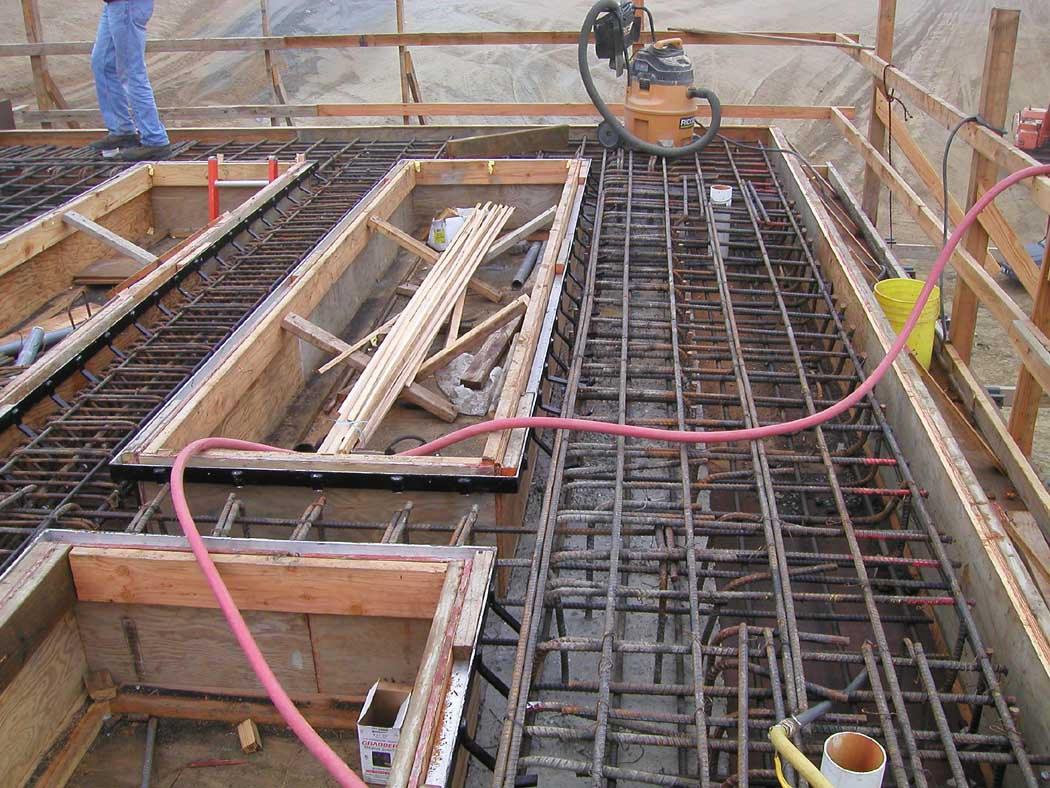 Rebar framework for concrete foundation with construction tools and a worker's legs visible.